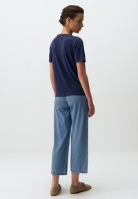 Een marineblauwe t-shirt met korte mouwen, gecombineerd met lichtblauwe wijde jeans. De outfit heeft een eenvoudig ontwerp met een gladde textuur.
