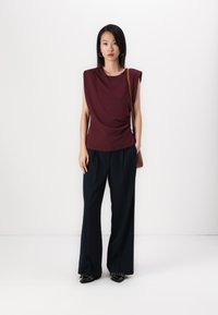 Burgundy draped top with shoulder pads and black wide-leg trousers. Black pointed shoes with a silver accent. Tan crossbody bag.
