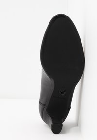 Semelle d'une chaussure à talons hauts en cuir noir avec une finition lisse, un bout pointu et un léger détail texturé. Taille 37 visible sur la semelle.