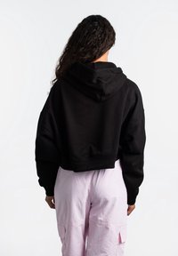 Zwarte cropped hoodie met capuchon en afgezakte schouders, gecombineerd met lichtroze cargobroek met zijzakken. Gladde katoenen stof.