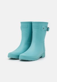 Bottes de pluie en caoutchouc turquoise avec une pointe arrondie, une semelle texturée et des accents de sangle réglables. Affiche le nom de la marque "Hunter" à l'avant.