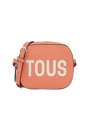 Bolso bandolera de piel melocotón con forma rectangular, que presenta letras en negrita en blanco "TOUS" y una correa ajustable en tono plateado.