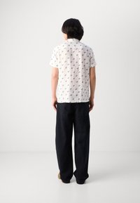Short-sleeve white shirt with blue floral pattern, paired with dark loose-fitting pants. Smooth fabric with a classic collar and button closure.