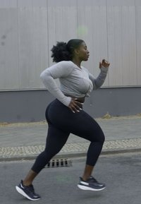 Athlete in gray long-sleeve crop top and black leggings, running on pavement. Textured fabric, fitted design, and functional athletic shoes.
