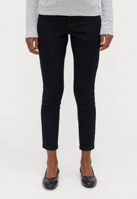 Calças de ganga pretas ajustadas, com uma cintura média, corte slim e punhos dobrados. Usadas com sapatos pretos rasos.