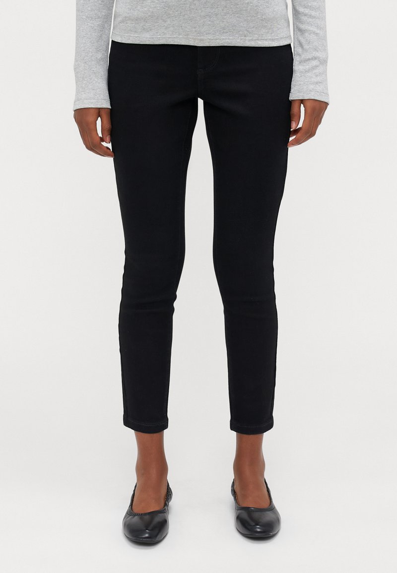 Calças de ganga pretas ajustadas, com uma cintura média, corte slim e punhos dobrados. Usadas com sapatos pretos rasos.