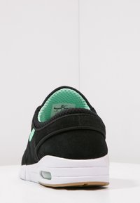 Czarne zamszowe sneakersy z zieloną siateczkową podszewką i białą środkową częścią. Posiadają zaokrąglony, wyściełany obcas oraz minimalistyczny design.