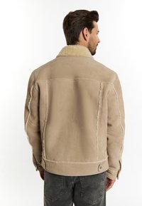 Beige Schaffelljacke mit weicher Textur, ausgestattet mit einem Stehkragen, kontrastierenden Nähten und Druckknopfdetails an der Taille.