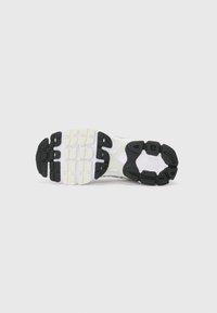 Semelle d'une chaussure de sport blanche avec une semelle extérieure en caoutchouc noir texturé, présentant un design de grip multi-patron et une semelle intermédiaire en mousse légère.