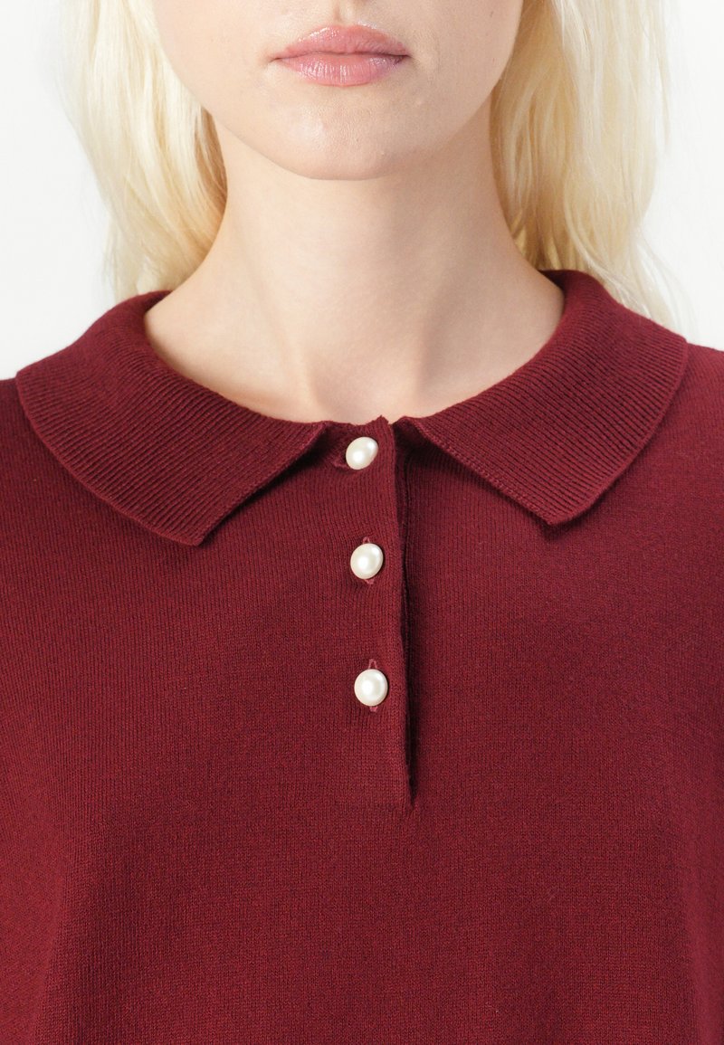 Burgundowy sweter o dzianinowej fakturze, z klasycznym kołnierzem i pięcioma guzikami przypominającymi perły z przodu do zapięcia.