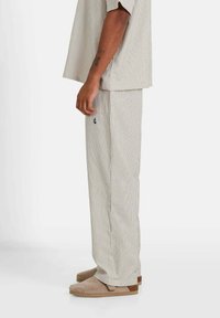 Ensemble de vêtements de détente rayé en beige clair et blanc, comprenant un haut à coupe ample et un pantalon assorti avec des poches latérales et une texture douce.