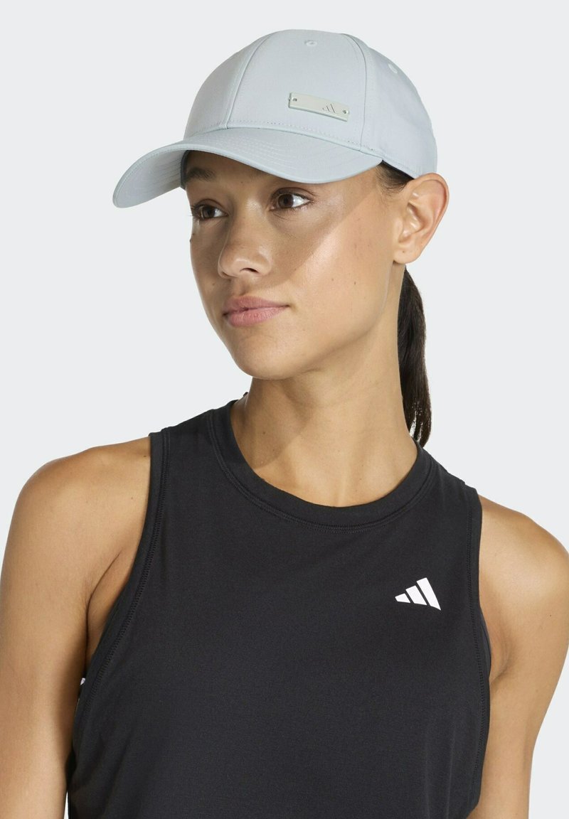 Woman wearing a light gray baseball cap and black sleeveless Adidas sports top, looking slightly to the side with neutral expression.
