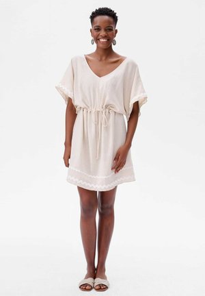 Beige kort jurkje met V-hals, trekkoord in de taille en golvende afwerking rondom de mouwen en de zoom. Gladde textuur, losse pasvorm en casual ontwerp.