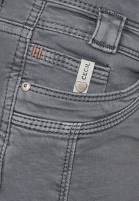 Jeans de mezclilla gris con un detalle de bolsillo que muestra costuras de cobre y una etiqueta blanca con la inscripción "CECIL". Incluye un bolsillo con botón plateado.
