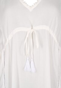 Túnica blanca fluida hecha de tela ligera, con escote en V, costuras decorativas y lazos de borlas en la cintura.