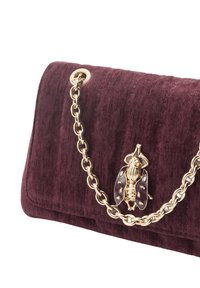 Aksamitna torebka w kolorze bordo z pasek na złotym łańcuszku i ozdobnym akcentem w kształcie owada z przodu. Teksturowana powierzchnia z prążkowanymi detalami.