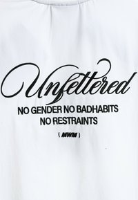 Camiseta de tela blanca con texto negro bordado. El diseño incluye la palabra "Sin ataduras" y frases adicionales debajo.