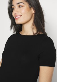 Tricou negru cu mânecă scurtă, confecționat dintr-un material moale. Dispune de un guler rotund, o formă ajustată și o textură netedă. Design simplu și clasic.