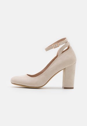 Beige ruskind højhælet sko med rundet tå, chunky hæl og justerbar ankelrem med guldlås.