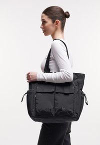 Svart tygväska i mjukt, hållbart material, med flera fickor, justerbar rem och en elegant, strukturerad design.