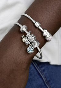 Srebrne zapestnice s čarami na temni koži, ki vsebujejo dekorativne predmete, bleščeče akcenti ter kombinacijo gladkih in teksturiranih površin.