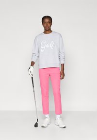 Gaišs pelēks sporta krekls ar uzrakstu "Golf" baltā krāsā, apvienots ar pieguļošām rozā biksēm. Baltas kurpes un golfa nūja lieliski papildina atletisko izskatu.