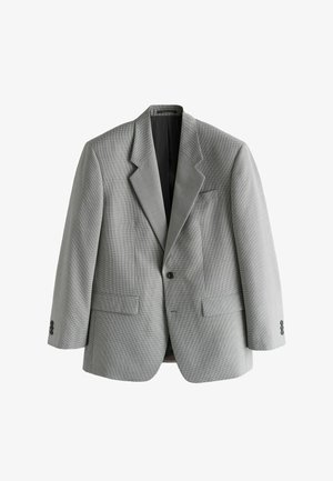 Bărbat care ajustează manșeta unui sacou cu model houndstooth, cu cămașă albă și cravată închisă la culoare texturată vizibile.