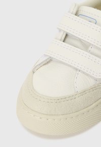 Hvit lær sneaker med borrelåser, semsket detaljer og beige gummisåle. Teksturert overdel med kontraststing og glatt finish.