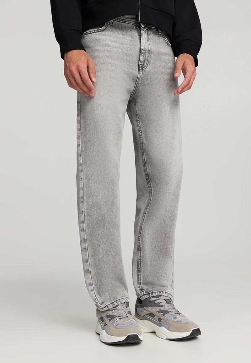 Jeans in denim grigio con un finish sbiadito, vestibilità dritta e cuciture a contrasto. Abbinati a sneaker grigie con dettagli in rete e suole in gomma.