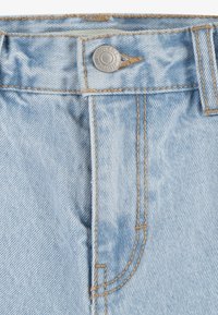 Jeans in denim azzurro chiaro con chiusura a bottone, caratterizzati da cuciture a contrasto color sabbia e un dettaglio sulla tasca frontale. La texture è liscia con un effetto sbiadito.