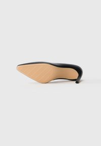 Black pointed-toe high heel shoe lying on its side showing a beige sole with grip stripes and a curved heel.