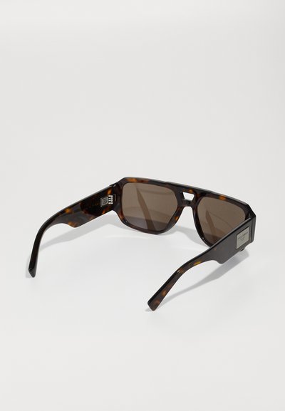Brown tortoiseshell sunglasses with a geometric frame, dark lenses, and subtle branding on the side. Smooth plastic texture, sleek design.