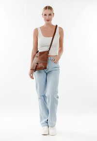 Sac en cuir marron bandoulière avec une poche zippée et une sangle réglable, associé à un jean bleu clair et un débardeur blanc côtelé.