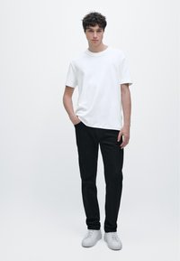 White cotton t-shirt and black jeans, model stands with one hand in pocket, white sneakers, smooth textures, neutral background.