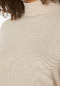 Pull à col roulé côtelé beige, doté d'une texture douce et d'une coupe ajustée. Motif subtil sur l'ensemble avec un col haut et serré.