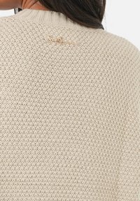 Pull en maille beige avec un motif texturé et un col côtelé. Présente un accent logo en ton doré au dos.