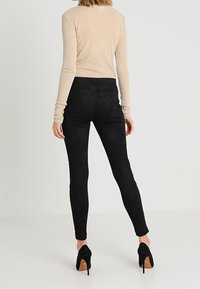 Leggings neri in suede con una vestibilità aderente, abbinati a una maglietta beige a maniche lunghe e scarpe con tacco alte nere. Texture liscia, senza motivi visibili.