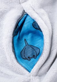Der weiße, flauschige Innenstoff der Tasche zeigt blauen Stoff mit schwarzen Illustrationen eines cartoonhaften Stingers im Wasser. Der Reißverschluss ist sichtbar.