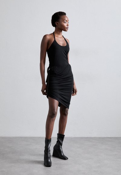 Rochie neagră cu decolteu halter și design plisat, având un accent lateral. Purtați cu botine negre, pe un fundal neutru.