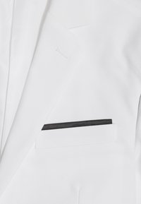 Biały żakiet o eleganckim designie, z teksturowanym materiałem i czarnymi wykończeniami kieszeni. Tkanina jest gładka z delikatnym połyskiem.