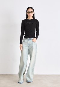 Crna košulja dugih rukava s logotipom "TOMMY JEANS", u kombinaciji s svijetloplavim oversized trapericama s poderanim rubovima i opuštenim krojem.