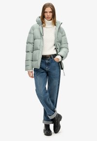 Puffet lysegrøn jakke med hætte, cremet strikketrøje, løse blå jeans og sorte snørebåndsstøvler. Har en afslappet pasform og oprullede ærmer.