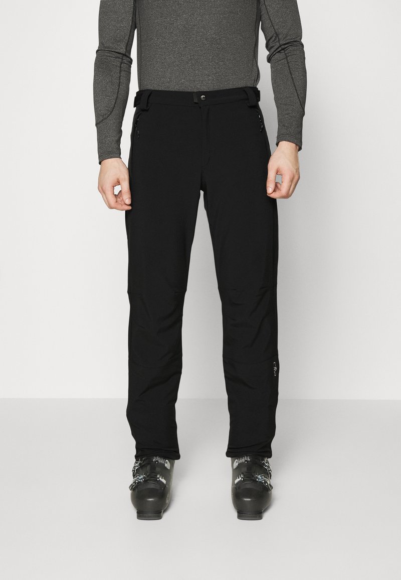 Black ski pants made of flexible fabric, featuring a slim fit, zip pockets, and reinforced hems, paired with black ski boots.