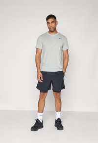 Maglietta Nike grigia con logo nero, abbinata a pantaloni corti sportivi neri con fianchi divisi. Indossata con calze bianche e scarpe da ginnastica nere.