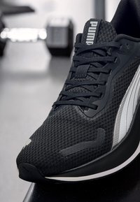 Schwarzer Sportschuh aus Mesh-Gewebe, mit einer texturierten Oberfläche, dicken Schnürsenkeln und einem markanten silbernen Streifen an der Seite.