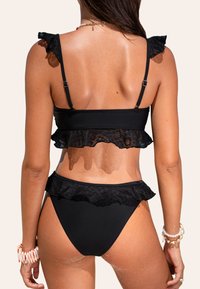 Bikini negro con acentos de volantes de encaje, con tirantes ajustables y un diseño ajustado. Tejido suave con una silueta elegante.