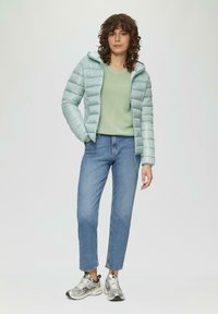 Lichtblauwe pufferjack met capuchon, gestructureerde groene trui, lichtblauwe jeans en zilveren sneakers, met een ontspannen pasvorm en ritsdetails.