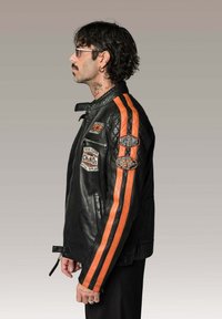 Veste de moto en cuir noir avec des rayures orange le long des manches. Présente des écussons sur le devant, une fermeture éclair et une coupe ajustée.