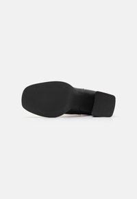 Semelle de chaussure en cuir noir avec une surface en caoutchouc texturée, dotée d'un large talon bloc et d'un design supérieur lisse et effilé.