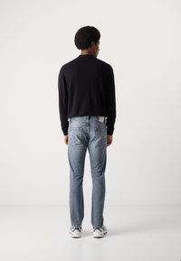Zwarte long sleeve shirt gecombineerd met lichtblauwe denim jeans. De jeans hebben achterzakken en een label bij de tailleband. Witte sneakers maken de look compleet.